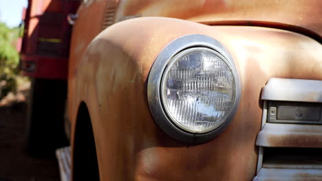 slow slide left along the front of an old rusty vintage truck fender with glass headlight and grill in the sunlight