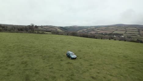 Dolly-back-aerial-drone-shot-of-farmer-driving-4x4-around-an-empty-field