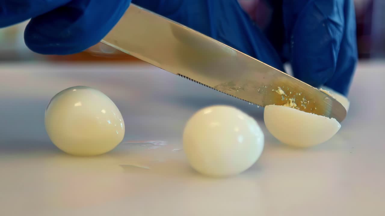 Hard-boiled eggs are halved with a large knife on a kitchen worktop