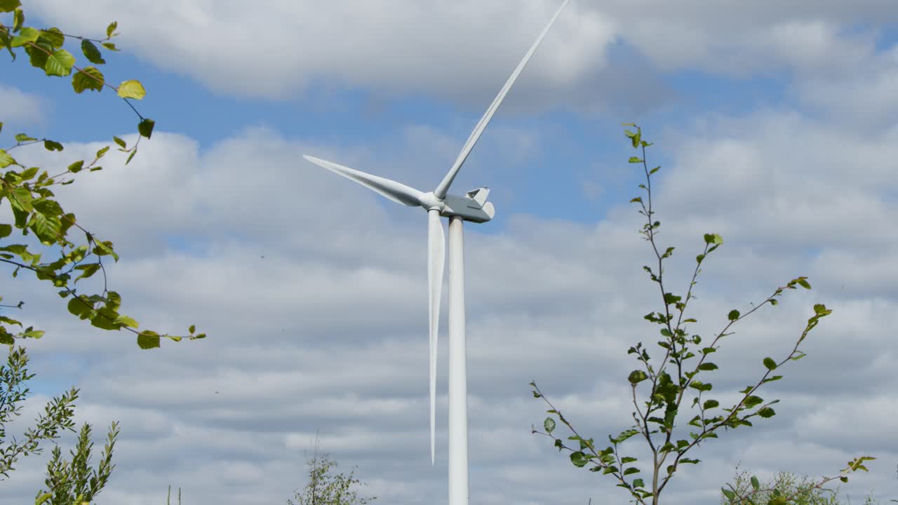Large wind turbine spins steadily in rural Highlands landscape, daylight, static camera, partly cloudy