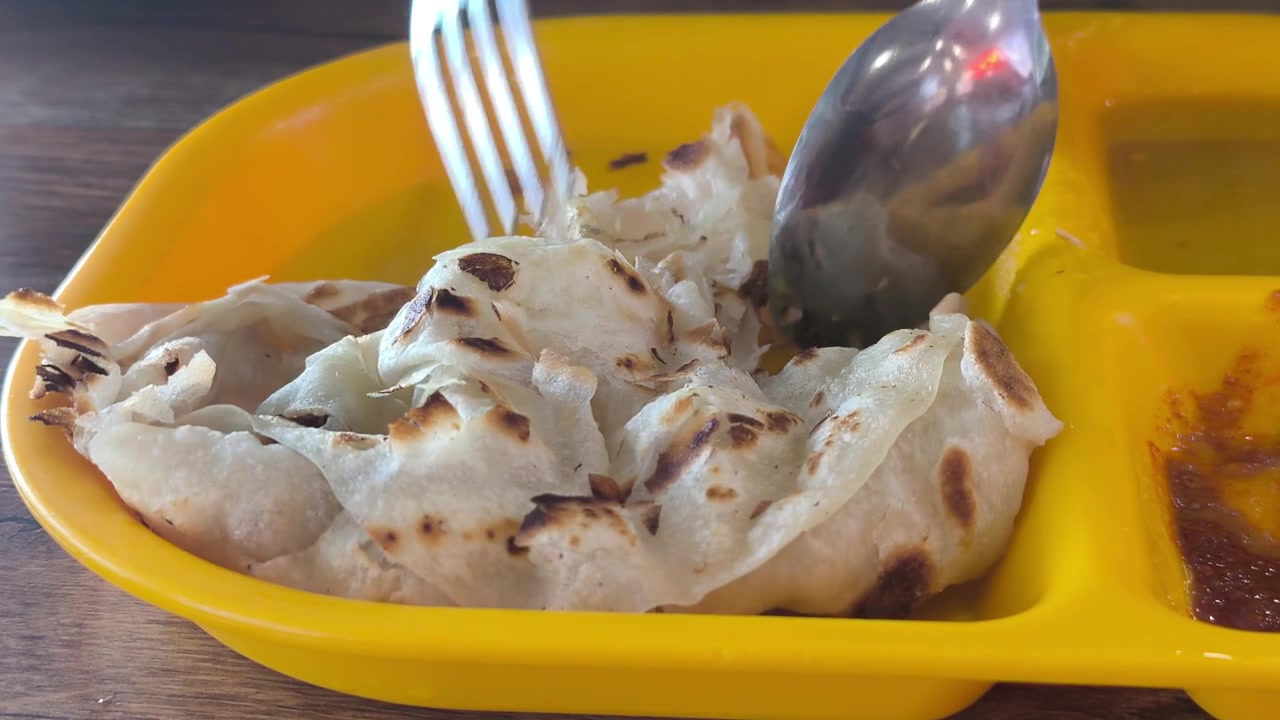 Un pezzo di classico roti canai è servito su un piatto con un saporito curry dhal. Questo rappresenta la preparazione base e fondamentale del piatto in Malesia. Rimane estremamente popolare per colazione.