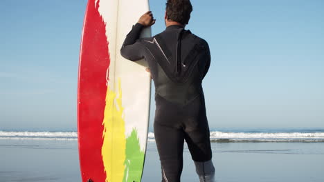 vertical shot of a male surfer in wetsuit with artificial leg leaning on the surfboard and standing in front of the sea