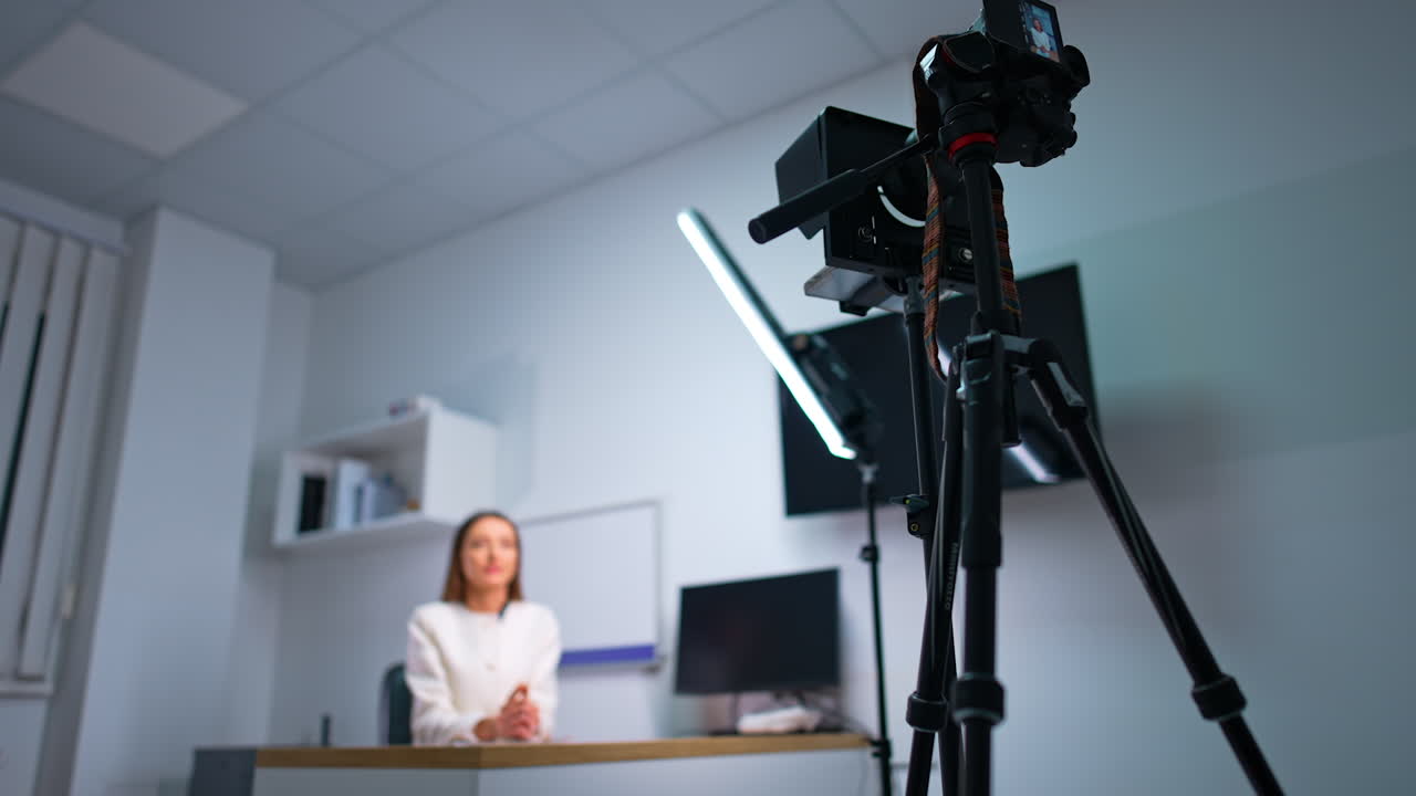 Blog presenter sits at desk talking to camera on tripod. Low angle view at the equipment for recording blog content. Blurred backdrop.