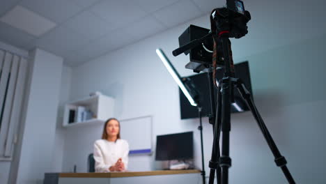 blog presenter sits at desk talking to camera on tripod. low angle view at the equipment for recording blog content. blurred backdrop.