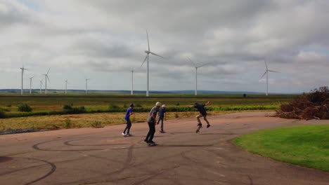 four kids skate boarding with backdrop of wind turbines, with clouds