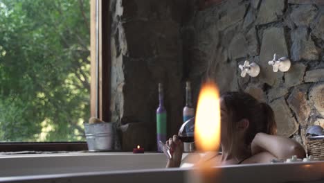 Joven-Mujer-Atractiva-Tomando-Un-Baño-Elegante-En-Un-Jacuzzi-Bebiendo-Vino-Con-Una-Gran-Ventana-Verde-De-La-Naturaleza