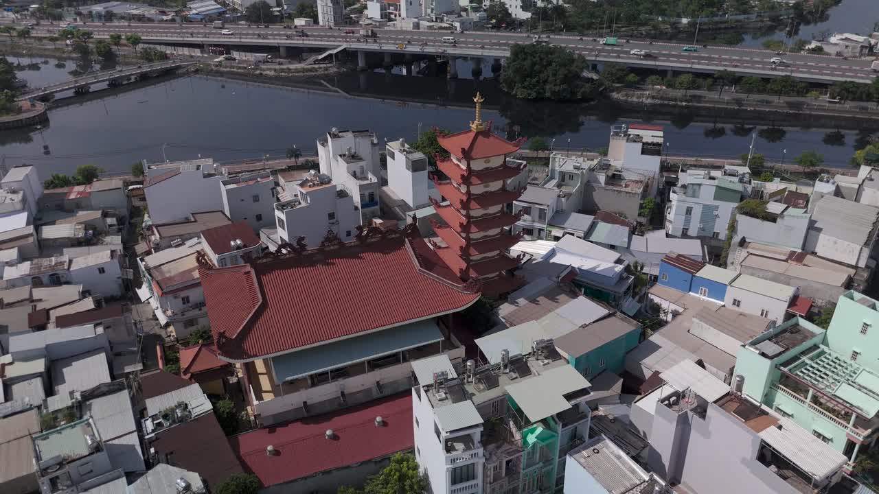 Orbit CCW drone view over Buddhist pagoda in busy urban area of Ho Chi Minh City, Vietnam on a sunny clear day featuring transportation infrastructure of main roads and canals in background
