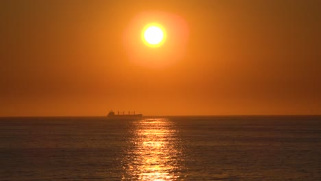 un buque de carga de contenedores distantes o un camión cisterna viaja contra el sol poniente al atardecer