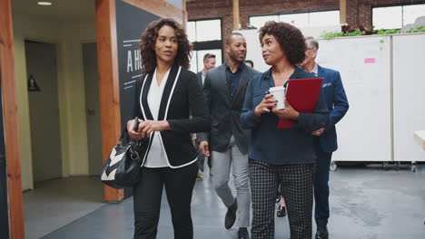 businesspeople arriving for work in busy modern open plan office walking towards camera