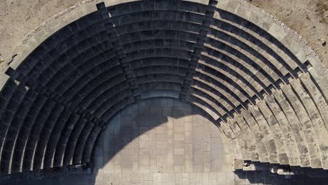 an ancient greek odeon, sinking top-down aerial view zooming in close on the stone seating