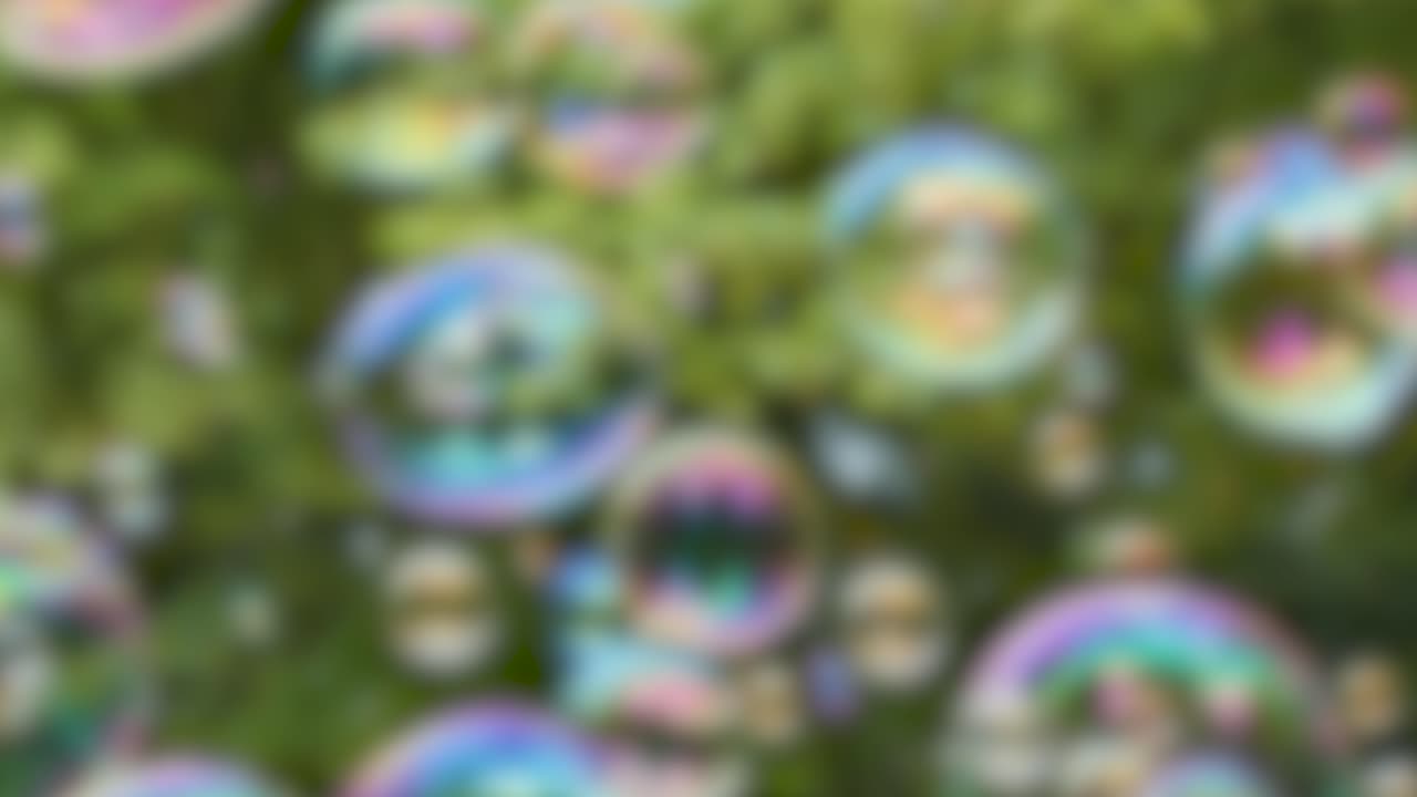 Colorful iridescent soap bubbles drift through the air against a soft bokeh green tree background
