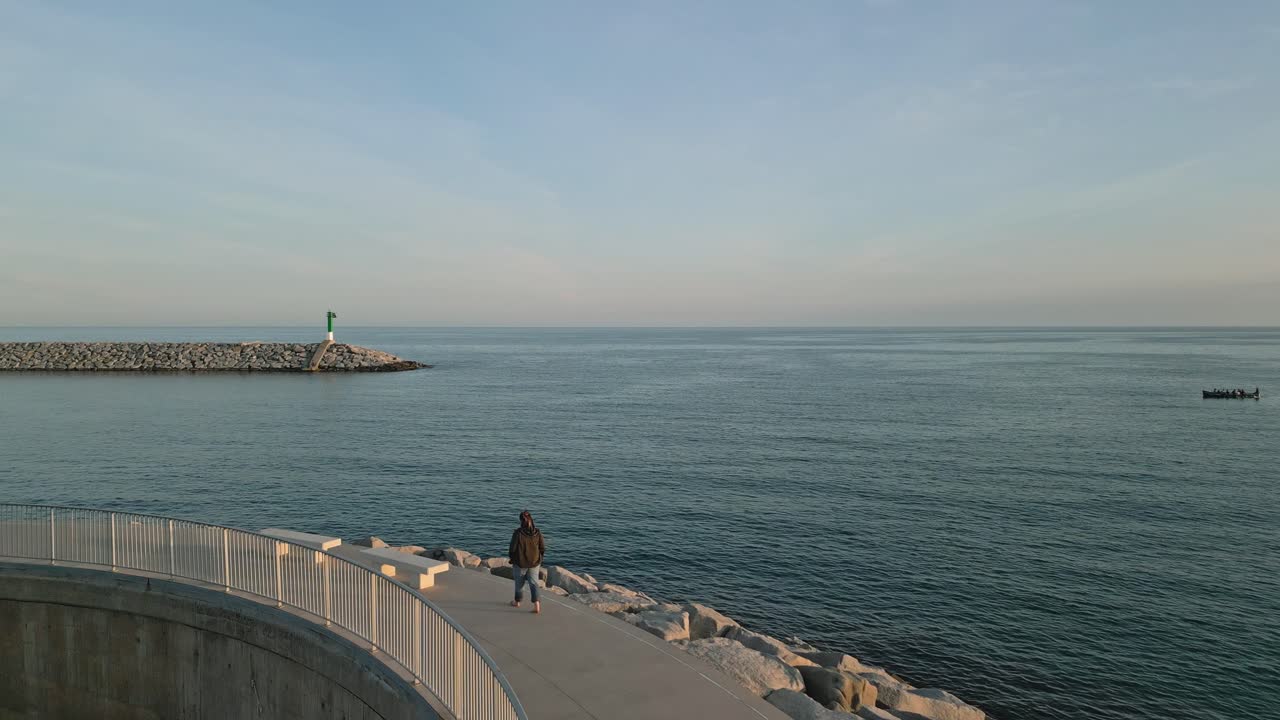 una mujer camina sola en el muelle de la playa, a orillas del mar de arenys de mar, cataluña disparo aéreo de avión no tripulado, turismo del mar azul, agua del océano