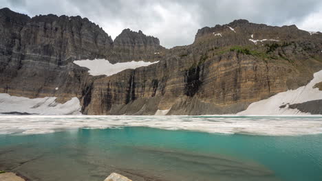 time lapse, glacier and glacial iceberg lake under steep cliffs, clouds and snow in landscape of glacier national park, mount grinnell