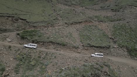 Aerial-tracks-rugged-tour-vehicles-driving-steep-mountain-pass-switchback