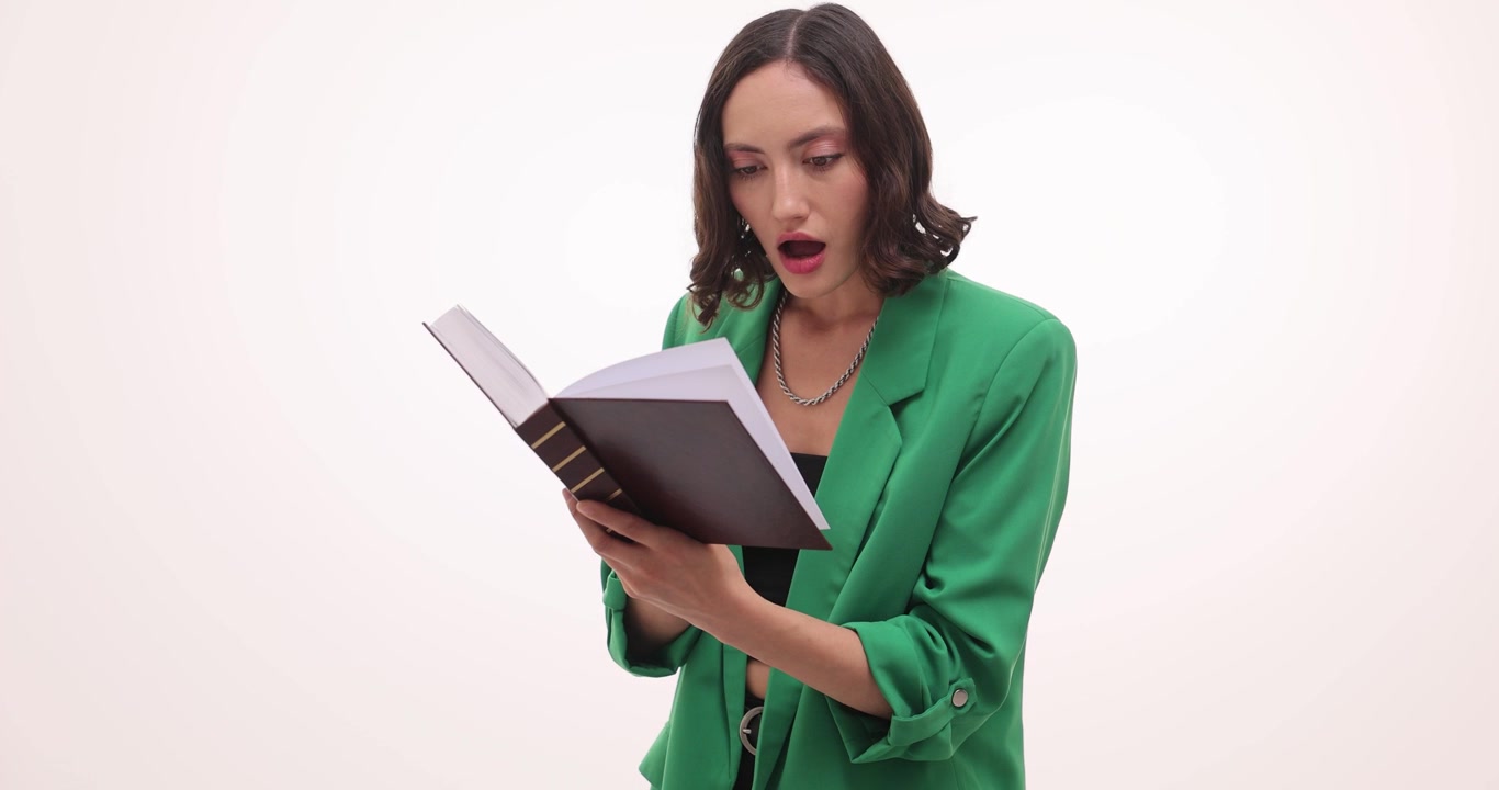 Mulher de verde lê um livro com expressão surpresa e espantada.