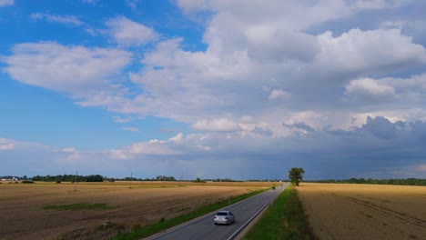 Drone Flight Over Golden Wheat Fields and Country Road on a Sunny Summer Day with Rainbow in the Sky Peaceful Latvian Countryside Aerial View