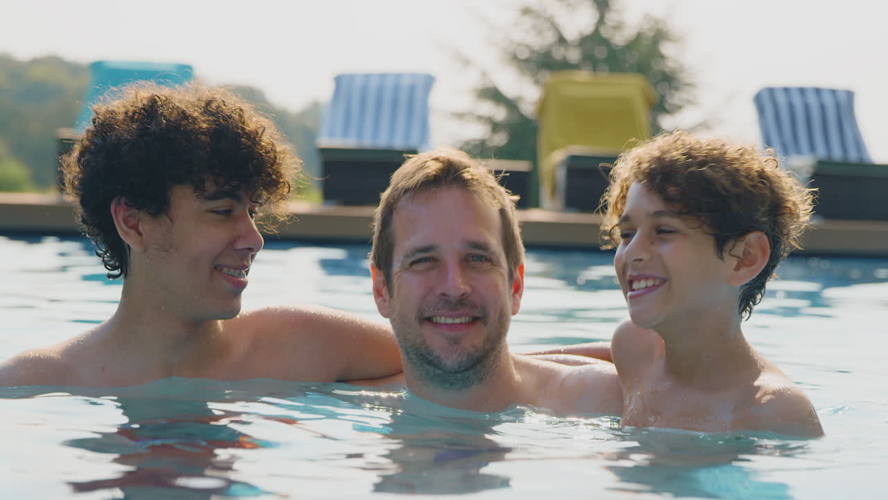 Ritratto di padre con i figli che si divertono in piscina all'aperto insieme durante le vacanze estive