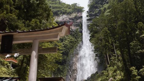 Nachi-Falls-with-no-people,-with-a-shrine-in-the-foreground,-and-a-giant-flowing-waterfall-surrounded-by-forest-in-the-background