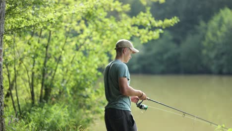 male angler gets his fishing rod out in murky lake surrounded by trees on sunny day