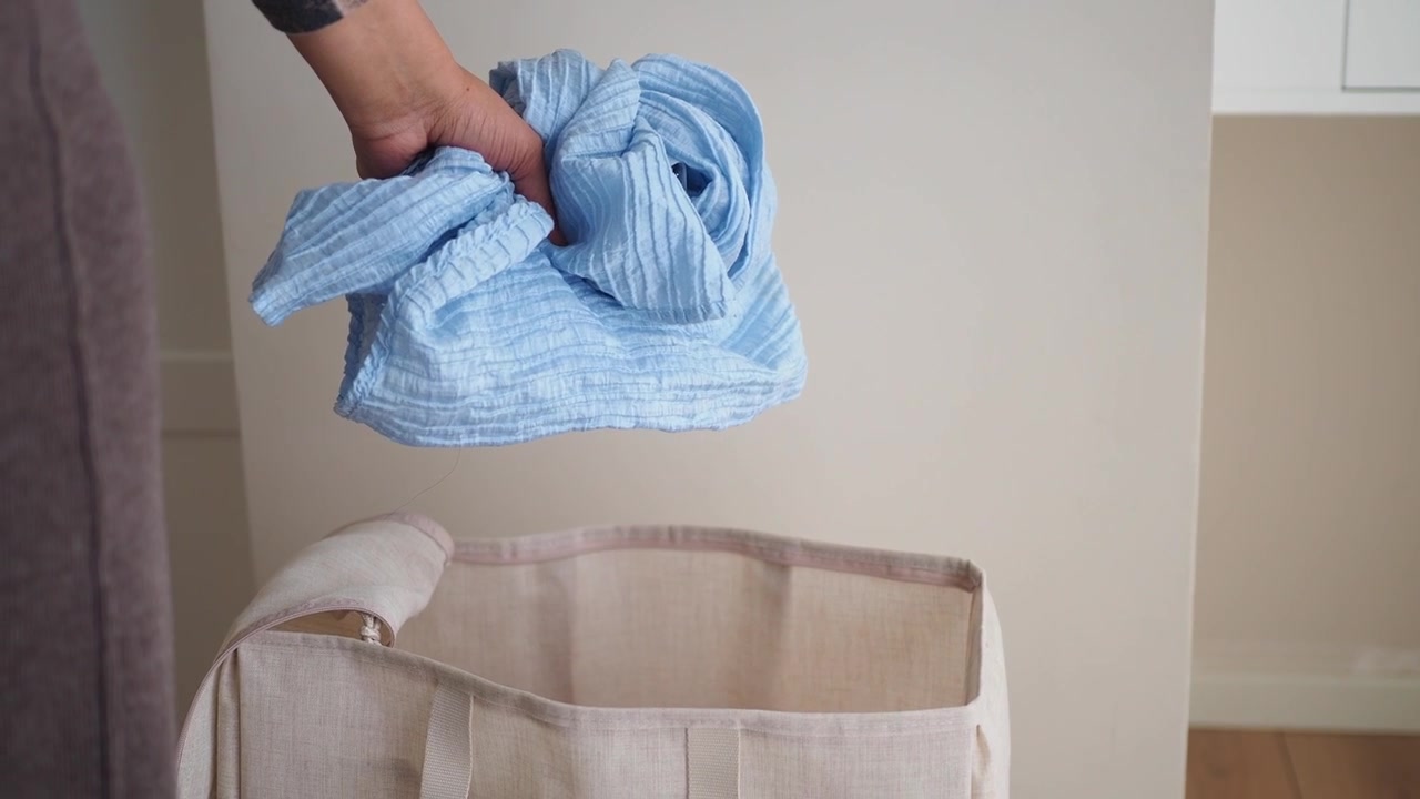 Person Placing Blue Fabric into a Laundry Basket and Closing It
