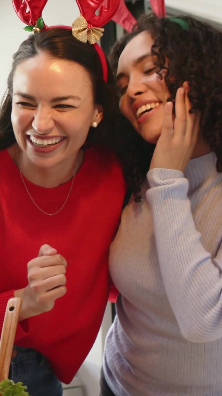 Video verticale: Donne che ridono e festeggiano con indumenti in maglia e corna di renna, sporgendosi sul bancone mentre servono l'insalata.