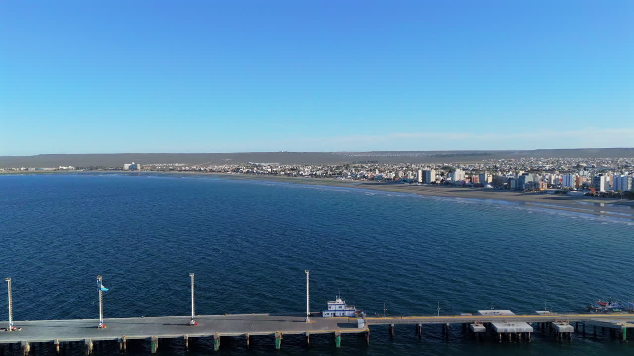 Aerial pullback of Puerto Madryn’s pier, highlighting vibrant ocean scenery and urban coastline in Patagonia, establishing