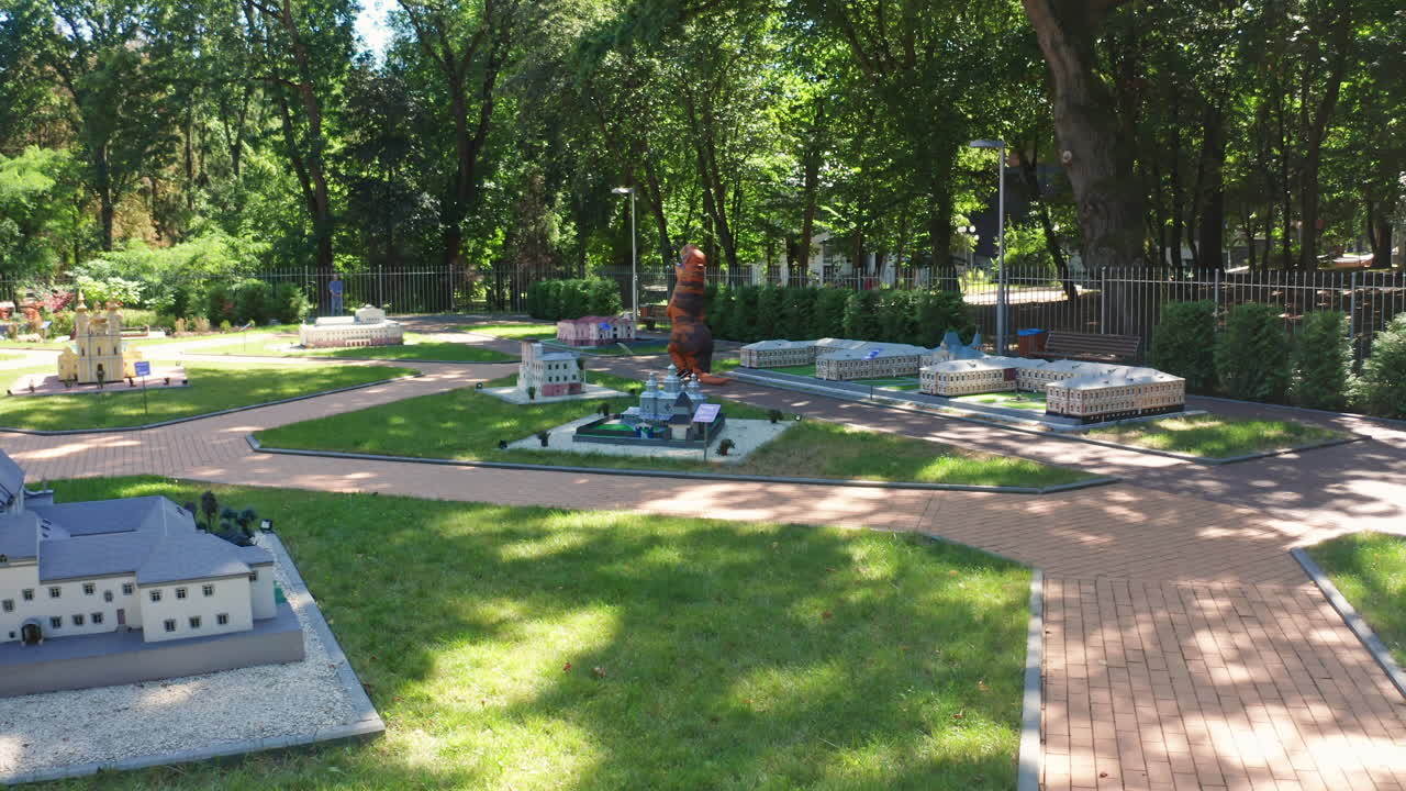 Person wearing Tirex dinosaur costume moving away. Dinosaur living miniature town museum outside. Summer day nature background.