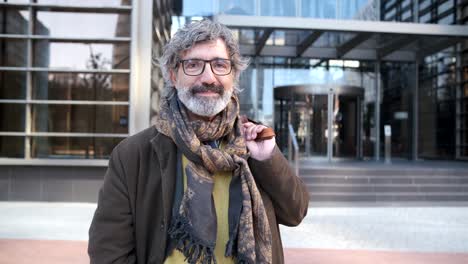 middle-aged man looking at the camera while posing in the financial district with an office building on background.