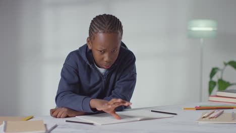 boy on asd spectrum at table at home struggling with concentrating on writing in school book 1