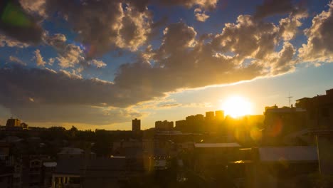 timelapse of dramatic sunset over cityscape with fluffy clouds, rain and golden sun in blue sky