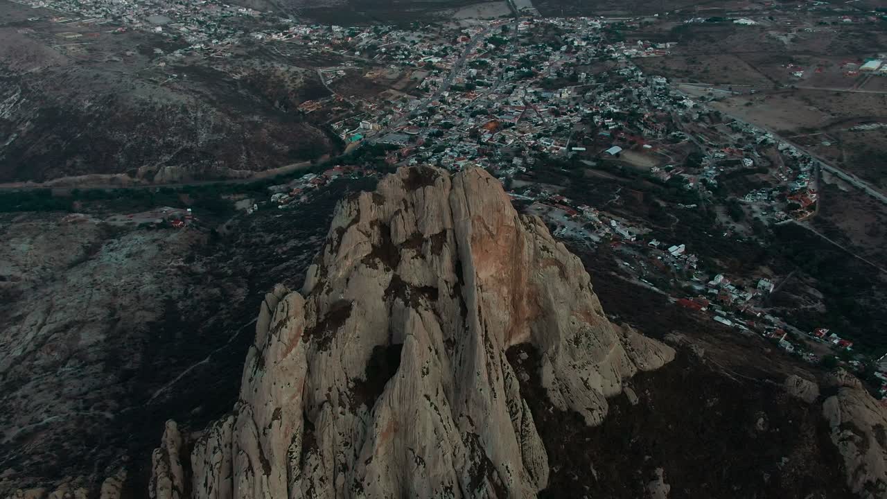 Panoramica aerea ravvicinata del monolito Peña de Bernal sopra la città con case e colline aride, Bernal, Querétaro, Messico.