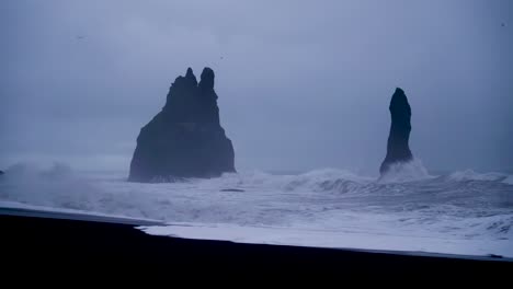 wide shot of black beach of reynisfjara during stormy crashing waves and mystical basalt boulders in iceland