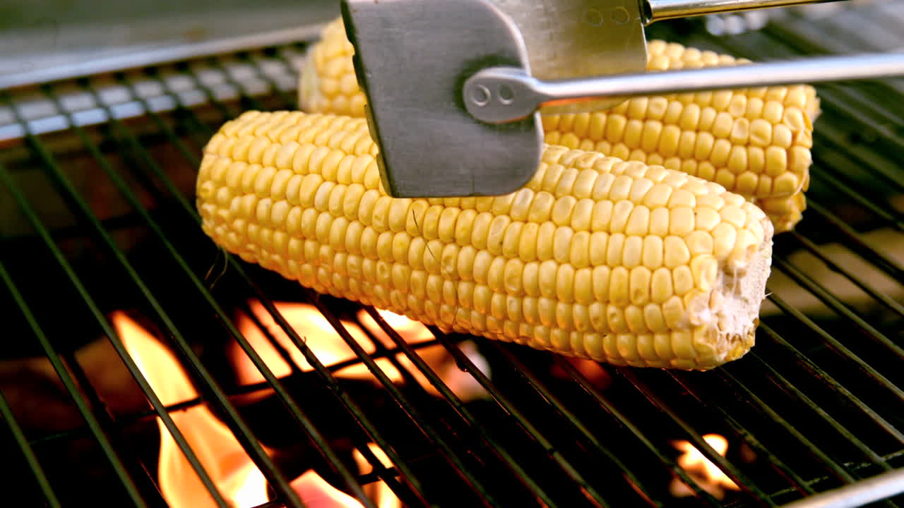 Corn on the cob being cooked on flaming barbecue