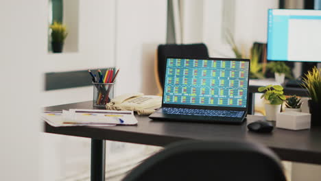 Paperwork-on-desk-next-to-laptop-in-office-showing-stock-exchange-values