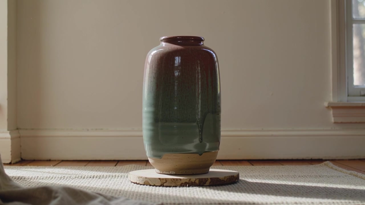 Piattaforma girevole che si avvia, ruotando un alto vaso in ceramica che rivela uno smalto lucido su un tappeto intrecciato a casa