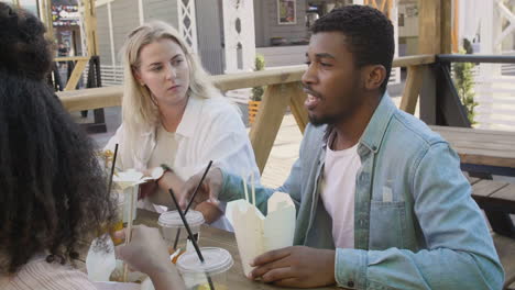 jovem conversando com seus amigos, sentado ao redor de uma mesa ao ar livre e comendo comida de rua