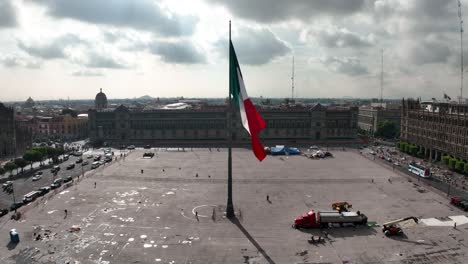 Aerial-view-towards-a-large-Mexican-flag-at-the-Zocalo-Square,-in-Mexico-city---slow-motion,-drone-shot
