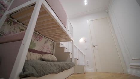 charming children's room featuring a bunk bed with pink upholstery, whimsical wallpaper, and a bright yellow ottoman, creating a playful yet elegant space