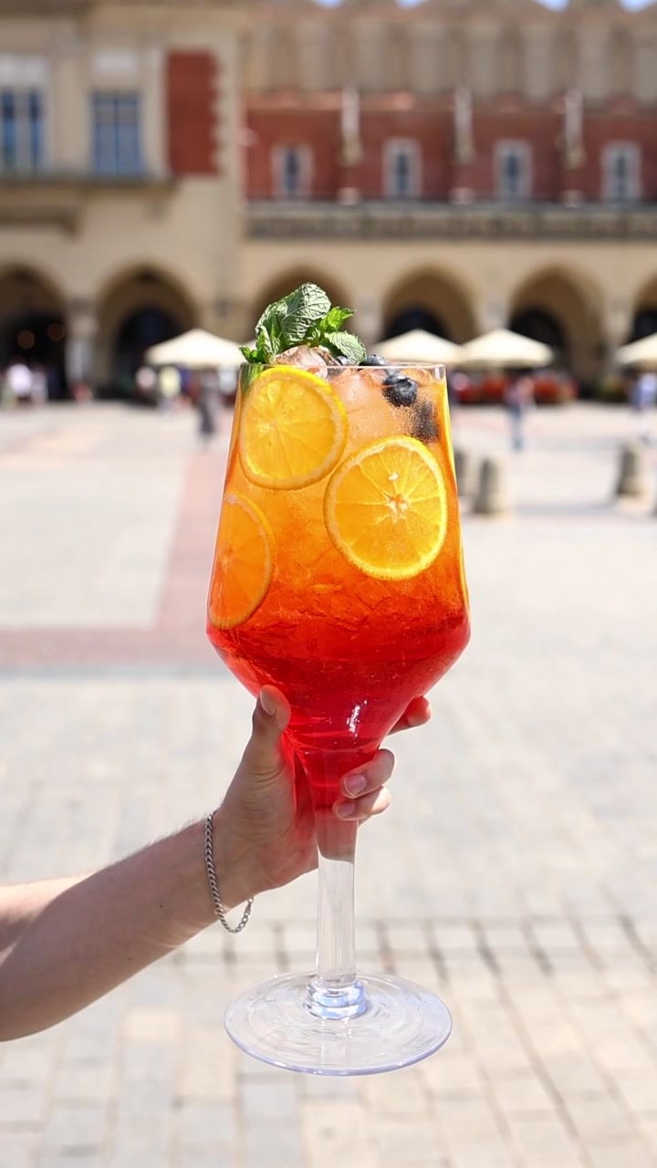 Mano che tiene un grande cocktail Aperol Spritz in una piazza pubblica