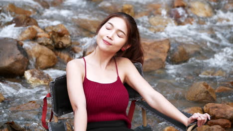 Asian-woman-in-red-sitting-on-a-chair-with-big-rocks-and-water-slow-splashing-for-relaxing-and-happiness-in-the-vacation-summertime