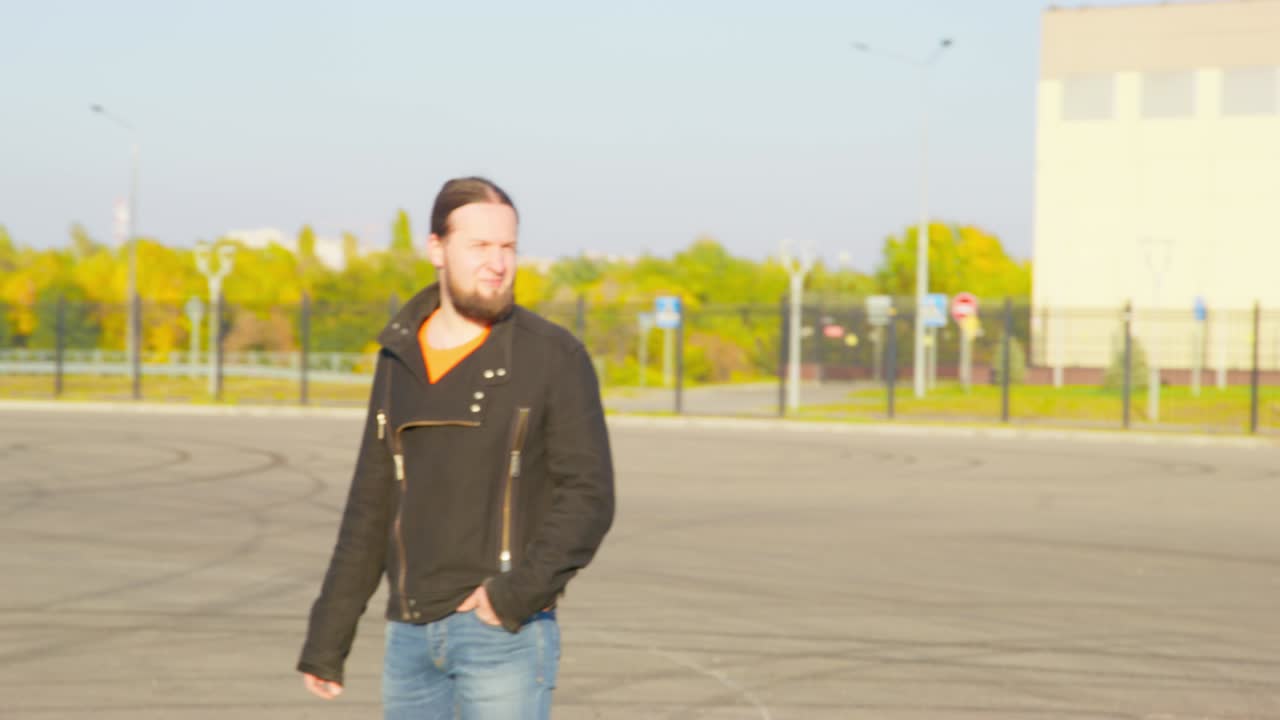 포니테일 (ponytail) 을 가진 프로 드라이버는 은 은 날 도시 전망에 대항하여 주차된 경주 자동차와 함께 드리프트를 위해 트랙을 검사합니다.