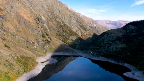 lac d'oô dam lake in the french pyrenees with low water level in the walls, aerial high altitude flyover shot