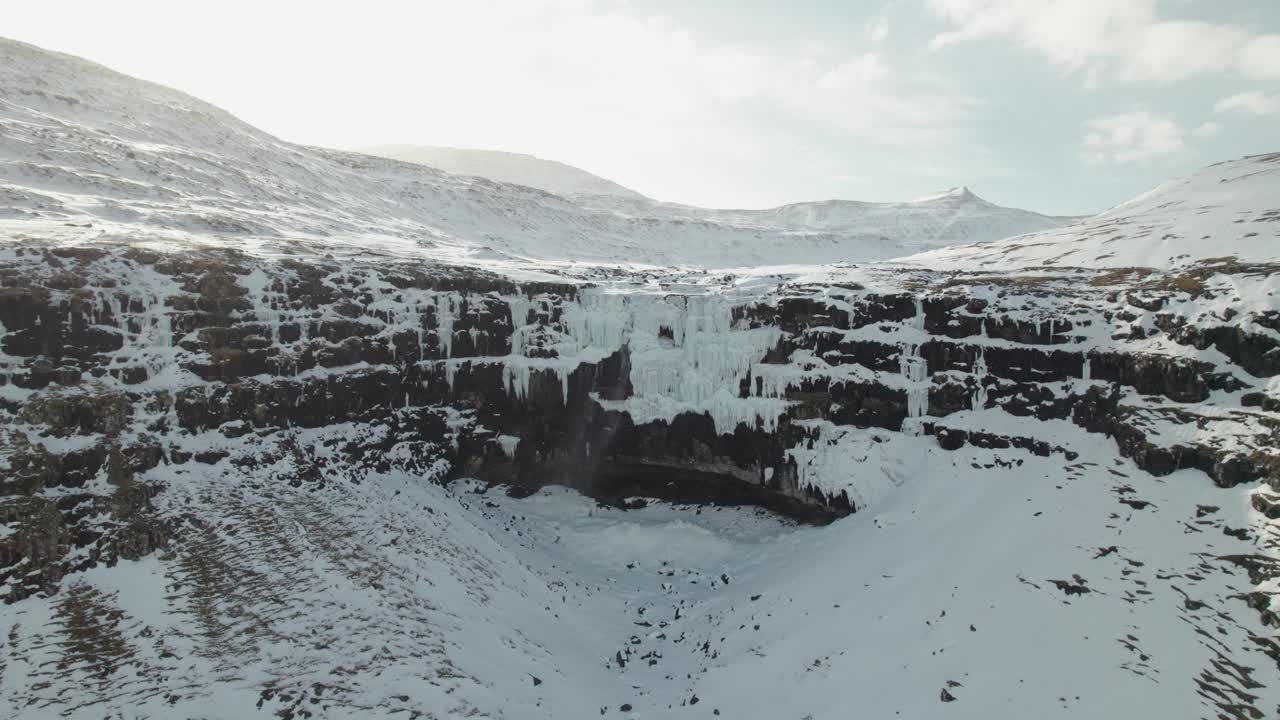 4K droneopptak fra luften av den 140 meter høye frosne fossen Fossurin I Fossá, den største fossen på Færøyene på Streymoy, på en kald og solrik vinterdag i et snødekket landskap
