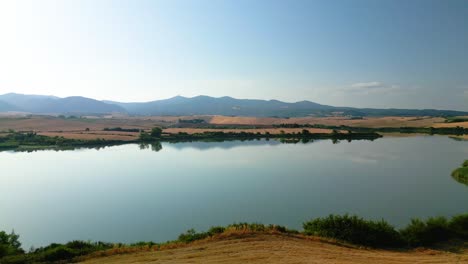 calm lake water mirrors the surrounding mountains and clear blue sky in the beautiful region of tuscany, italy, creating a peaceful and scenic landscape