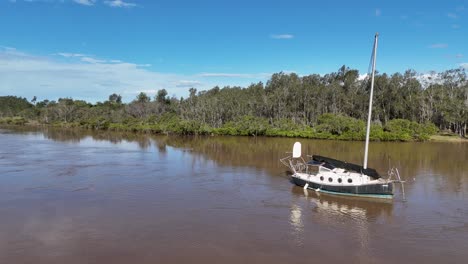 Aerial view of stationary sailboat on calm river near lush green banks in daylight