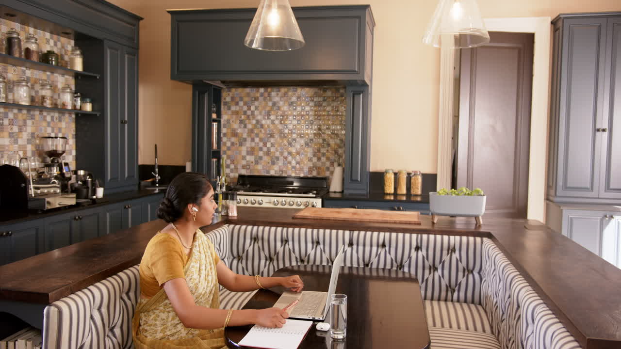 Working from home, Indian woman in traditional sari using laptop in kitchen
