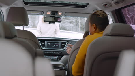 man closing car hood after checking engine, while his two friends sitting in the car on a winter day