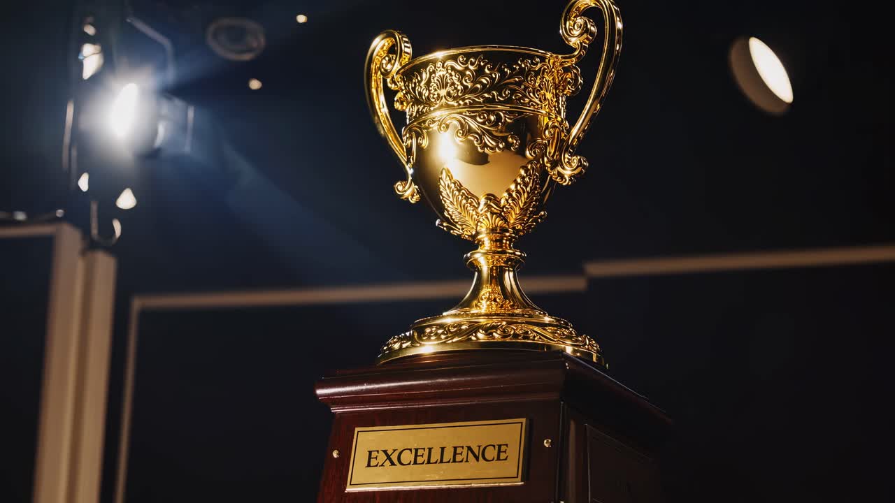 A close-up, low-angle shot of a golden trophy labeled 'Excellence' against a dark background