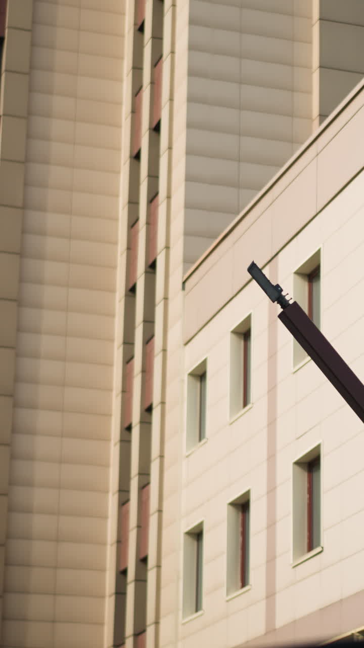 fachada beige de un edificio con ventanas, rótulo vertical y primer plano de la viga de soporte en ángulo del revestimiento del panel y cristales captando la luz del sol de la tarde, líneas geométricas nítidas y juego de sombras, ideal