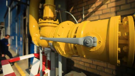 close-up of a yellow gas pipeline with valves on a sunny day, blurred background with person waiting